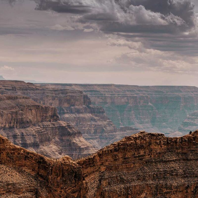 A vast, multi-layered canyon stretches under a dramatic, cloudy sky.