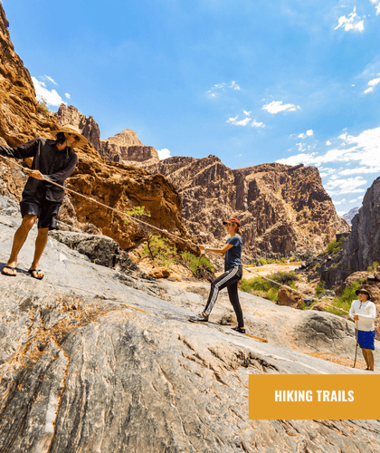 Two people use ropes to navigate a rocky incline on a hiking trail in a canyon.