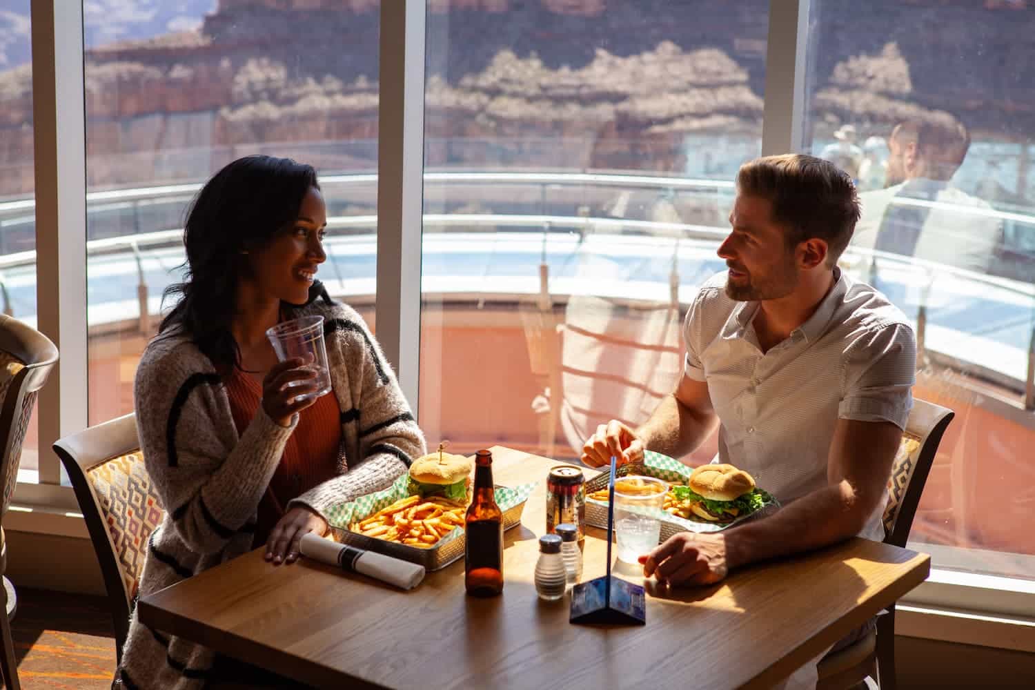 A couple eating burgers and fries at a restaurant with large scenic windows.