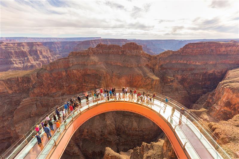 Crowds walking on the curved glass-bottom Grand Canyon Skywalk, suspended over deep canyon cliffs with breathtaking desert landscape in the background.
