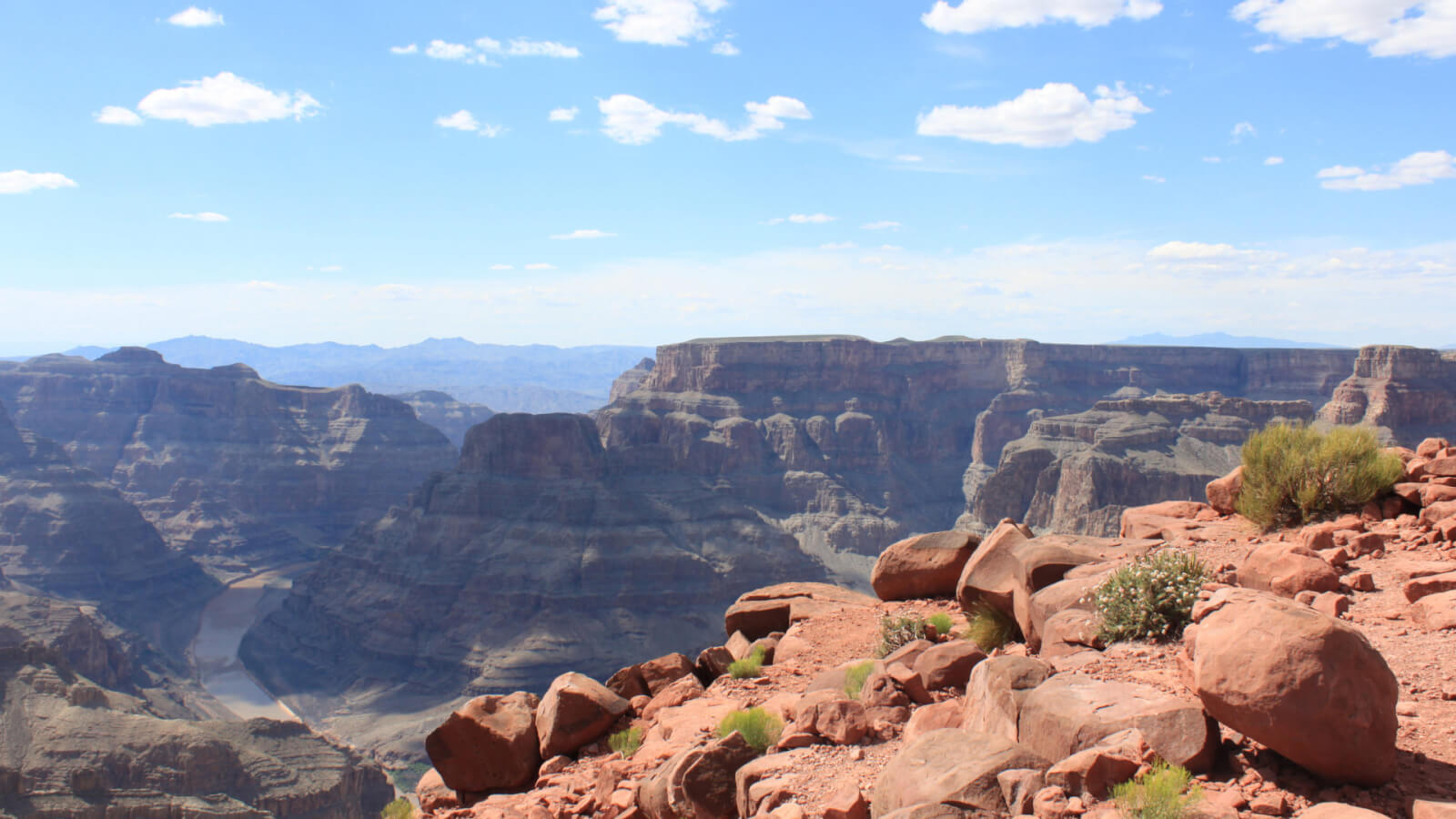 An expansive view of the Grand Canyon West Rim on a clear day with a few puffy white clouds overhead.