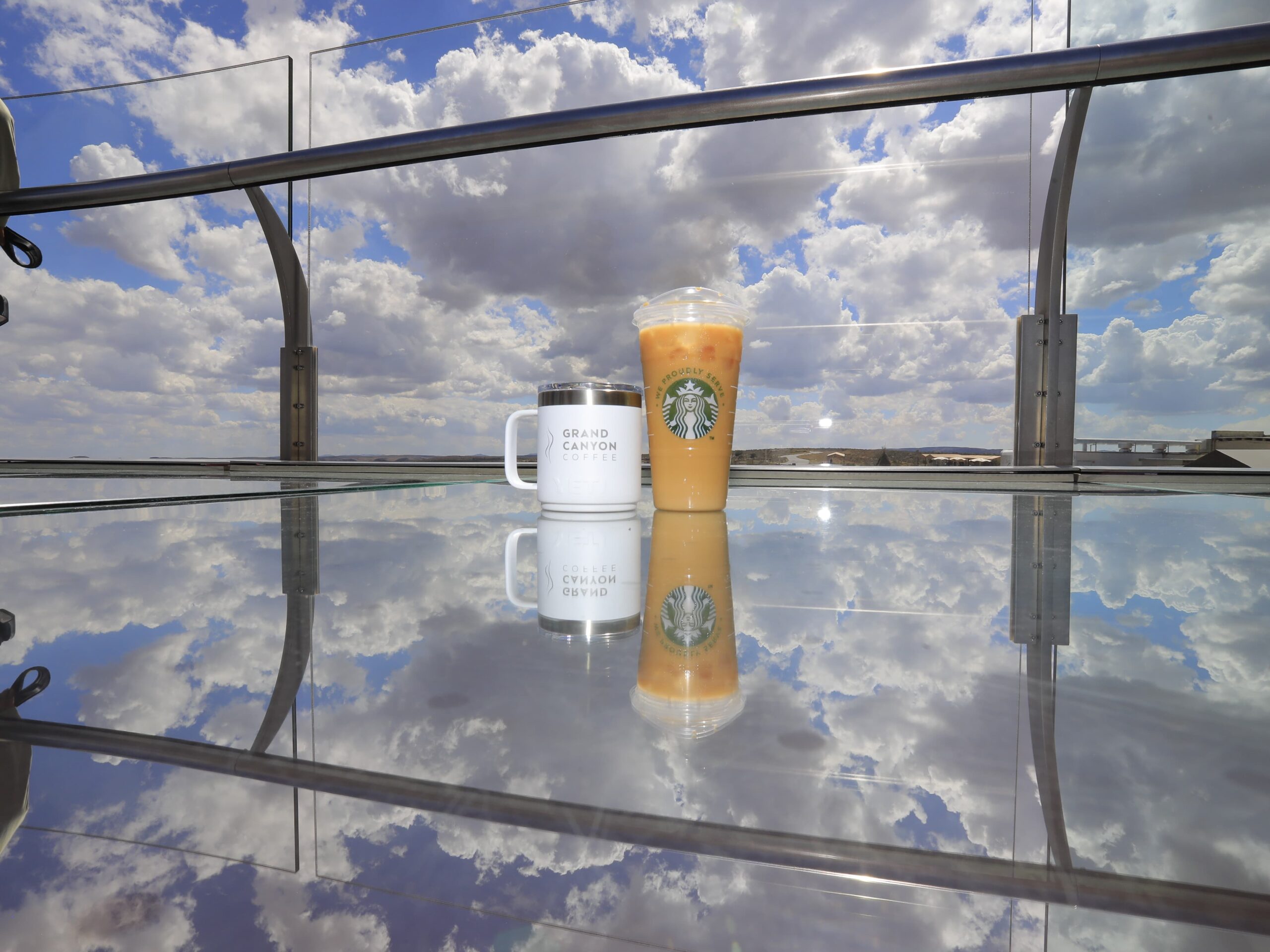 Grand Canyon Coffee A Grand Canyon Coffee mug and a Starbucks iced coffee sit on the glass floor of the Grand Canyon Skywalk, with the cloudy blue sky perfectly reflected on the surface