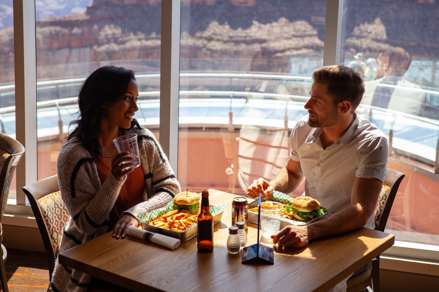 The Ultimate Vegas to Grand Canyon Road Trip Itinerary A couple eating burgers and fries at a restaurant with large scenic windows.