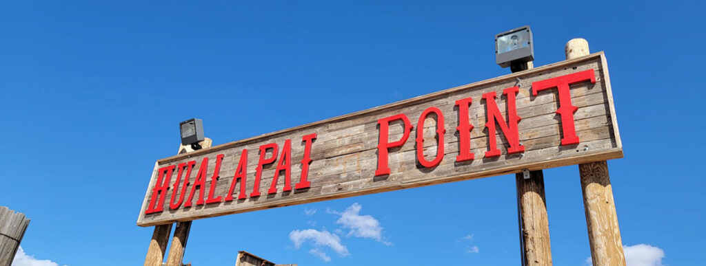 Dinge die zu tun sind A wooden sign with "HUALAPAI POINT" in red letters is against a clear blue sky.